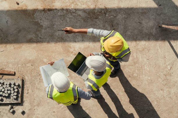 Three construction workers wearing hard hats and safety vests, engaged in concrete testing at a construction site.
