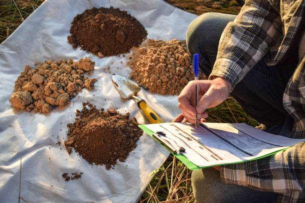 A man writes on a clipboard while examining soil, illustrating a geotechnical soil investigation process.
