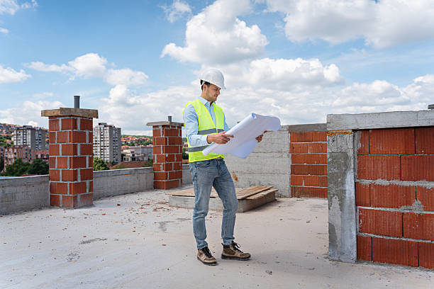 A man stands with a shovel outside a building related to concrete testing companies.

